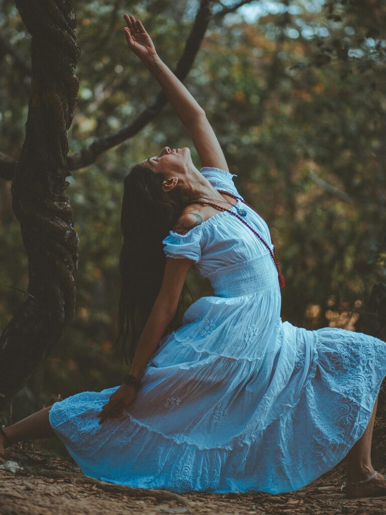 A woman in a blue dress performs a yoga pose amidst nature's tranquility. Sol by Luna Philosophy